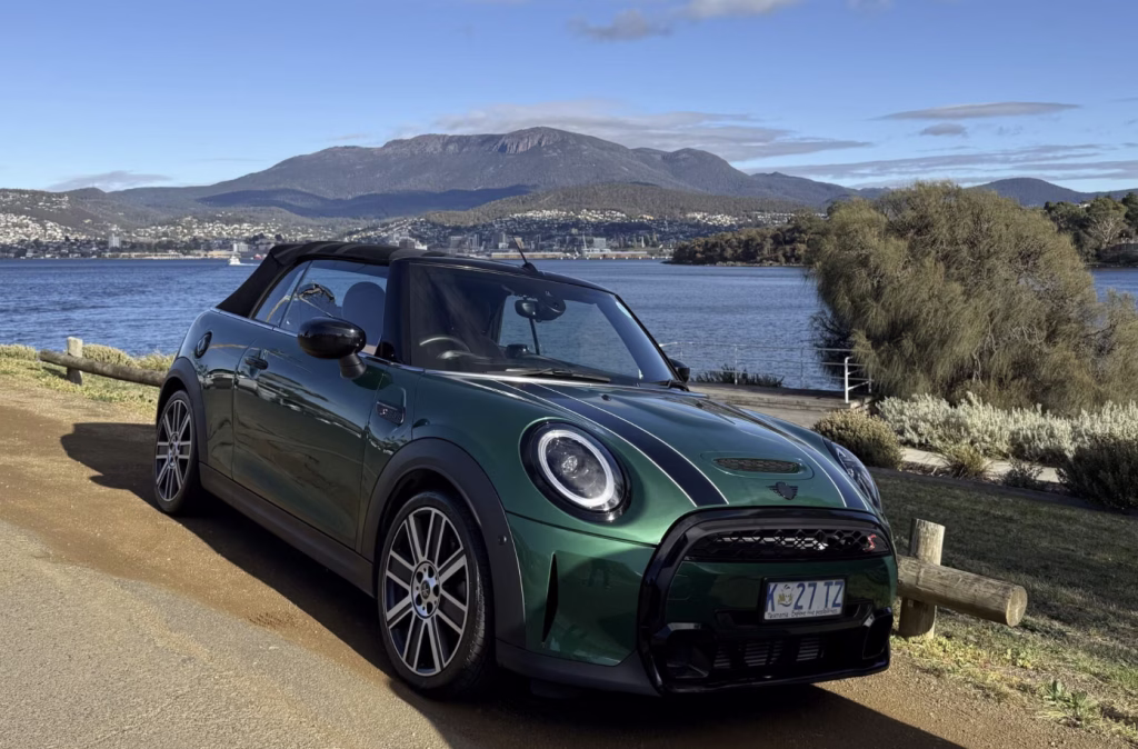 A green Drive Car Hire MINI Cooper convertible stands parked in front of Mt Wellington / kunanyi.
